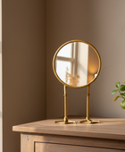 Gold vanity mirror on a wooden surface with a plant in the background
