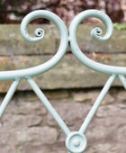 Decorative metal railing with scroll design in front of a stone wall.