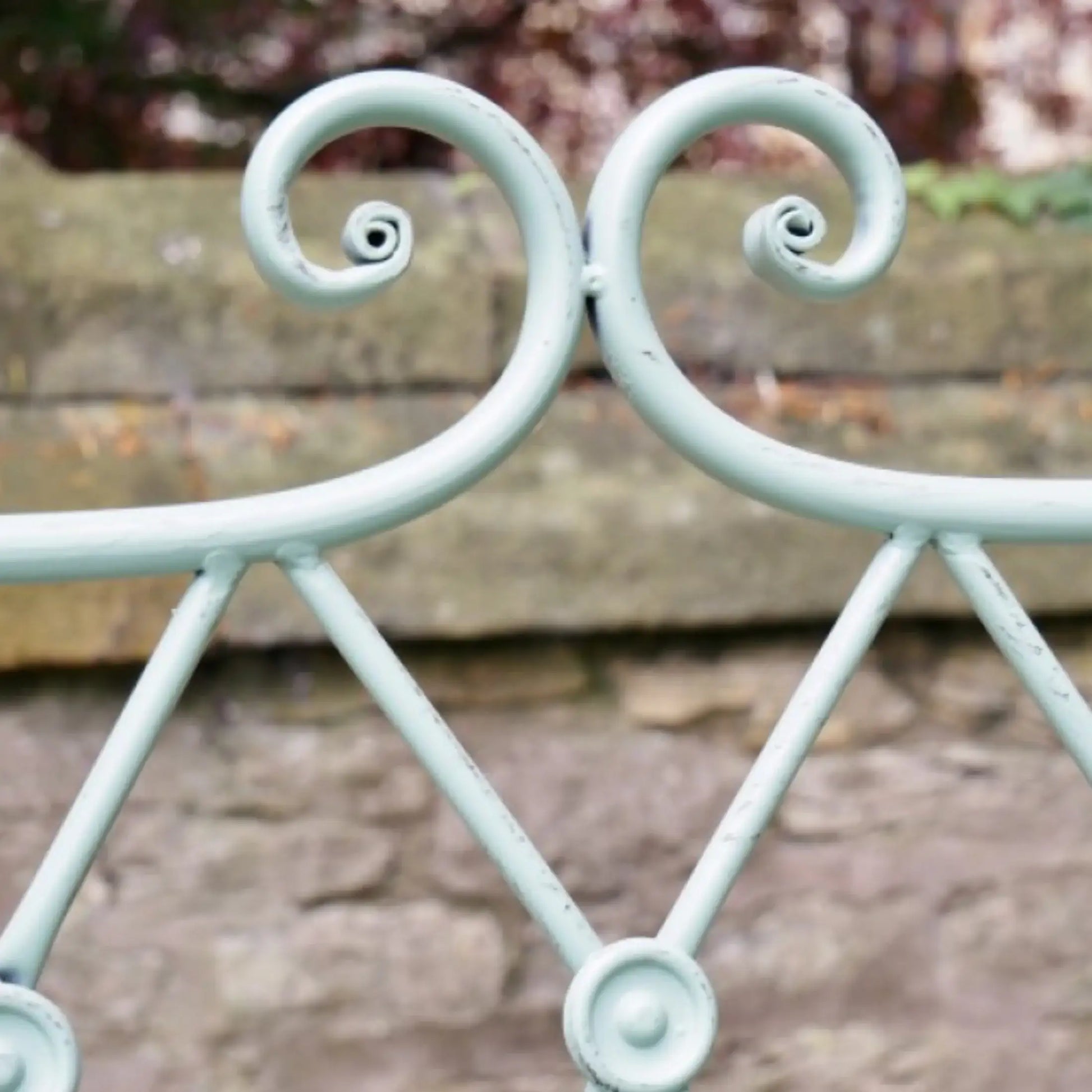 Decorative metal railing with scroll design in front of a stone wall.