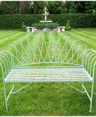 Decorative metal bench on a grassy lawn with a fountain in the background