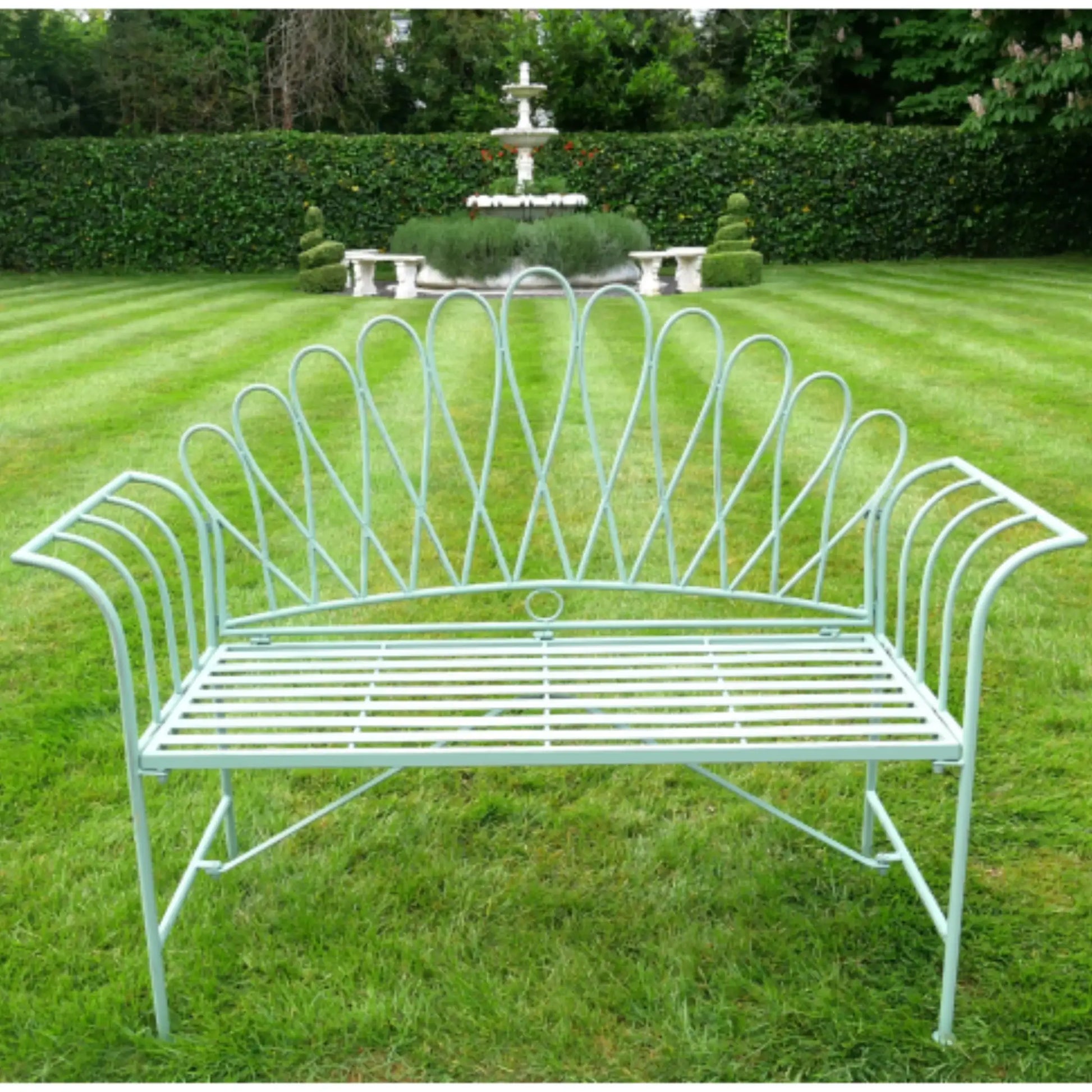 Decorative metal bench on a grassy lawn with a fountain in the background