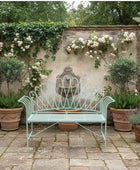 Decorative garden bench in a lush, floral setting with potted plants and a stone wall.
