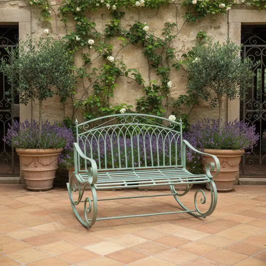 Decorative metal bench in a garden setting with potted plants and a stone wall.