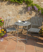 Outdoor patio with metal chairs, table, and potted flowers against a stone wall.