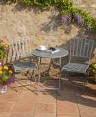 Outdoor patio set with table and chairs against a stone wall, surrounded by flowers.