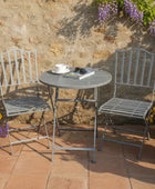 Outdoor patio set with two chairs and a table against a stone wall with flowers.