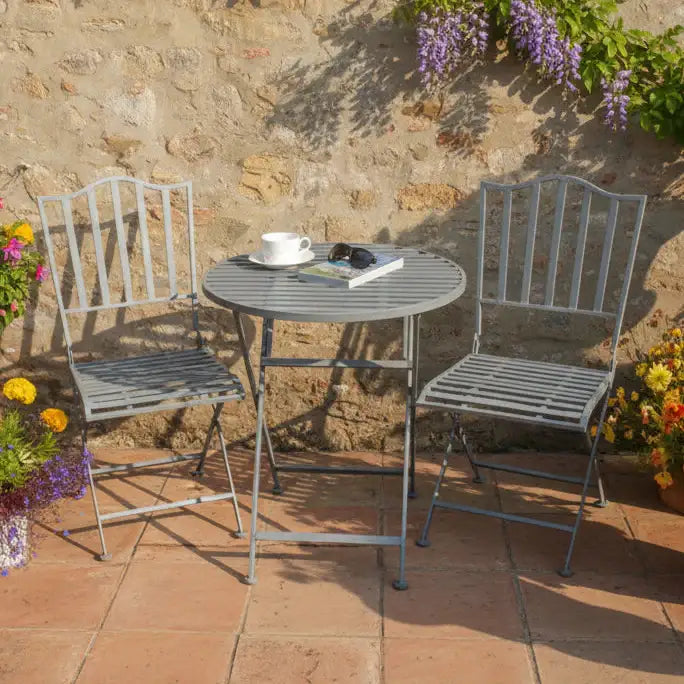 Outdoor patio set with two chairs and a table against a stone wall with flowers.