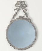 Decorative round mirror with intricate frame and bow on a white background