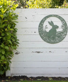 White wooden gate with a green circular design featuring a rabbit, surrounded by greenery.