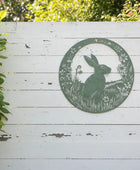 Decorative metal wall art of a rabbit in a circular frame on a white wooden background.