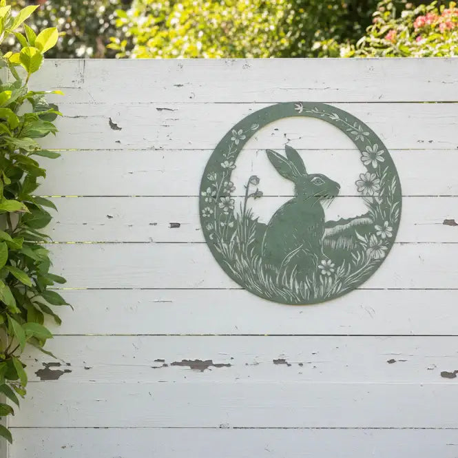 Decorative metal wall art of a rabbit in a circular frame on a white wooden background.