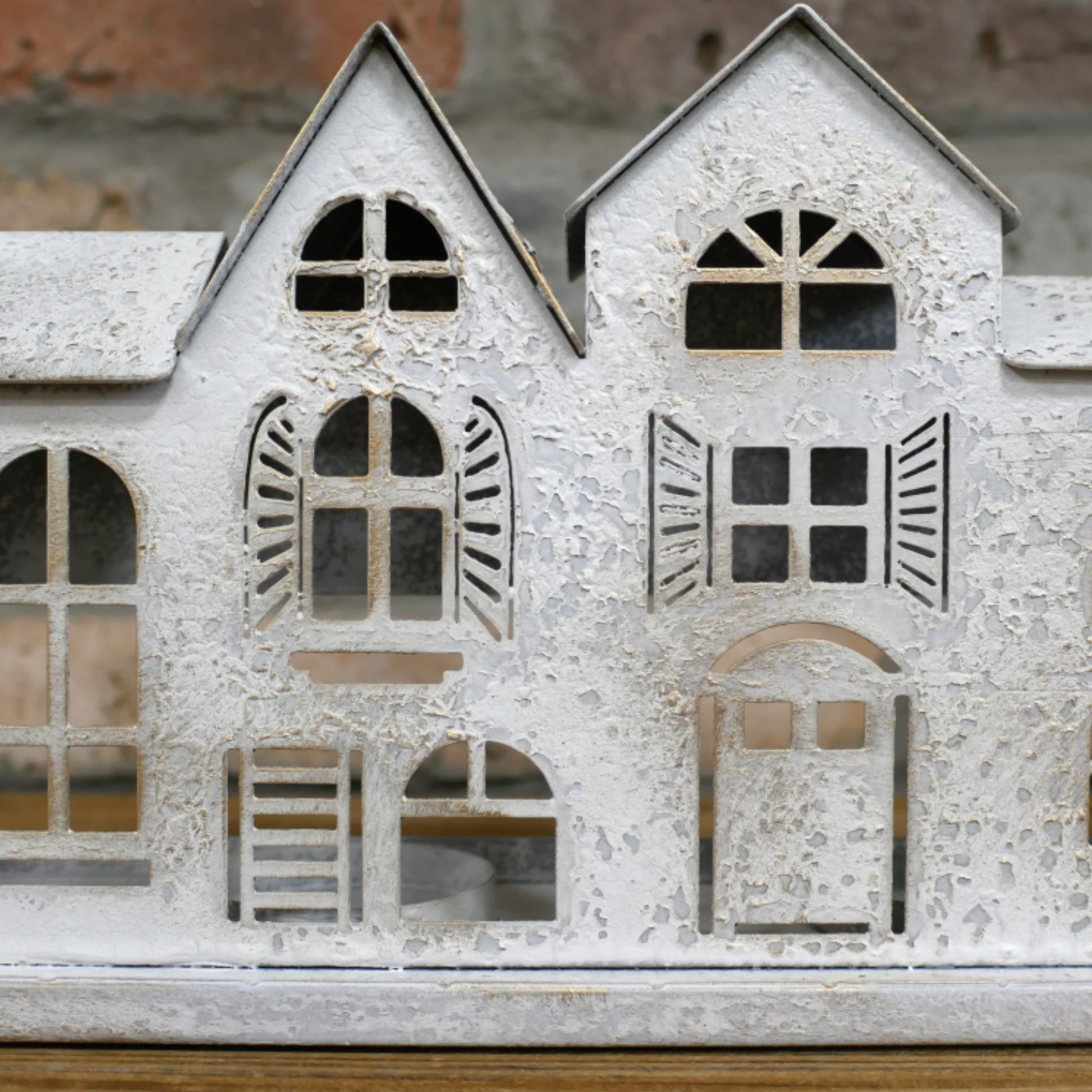 Decorative metal house model with cut-out windows and shutters on a wooden surface.