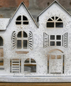 Decorative metal house model with cut-out windows and shutters on a wooden surface.