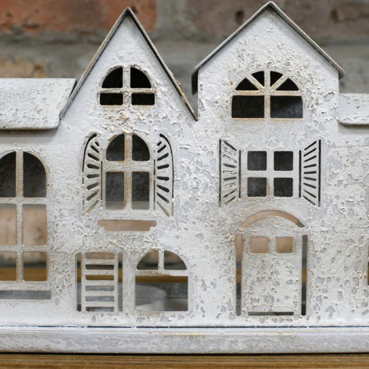 Decorative metal house model with cut-out windows and shutters on a wooden surface.