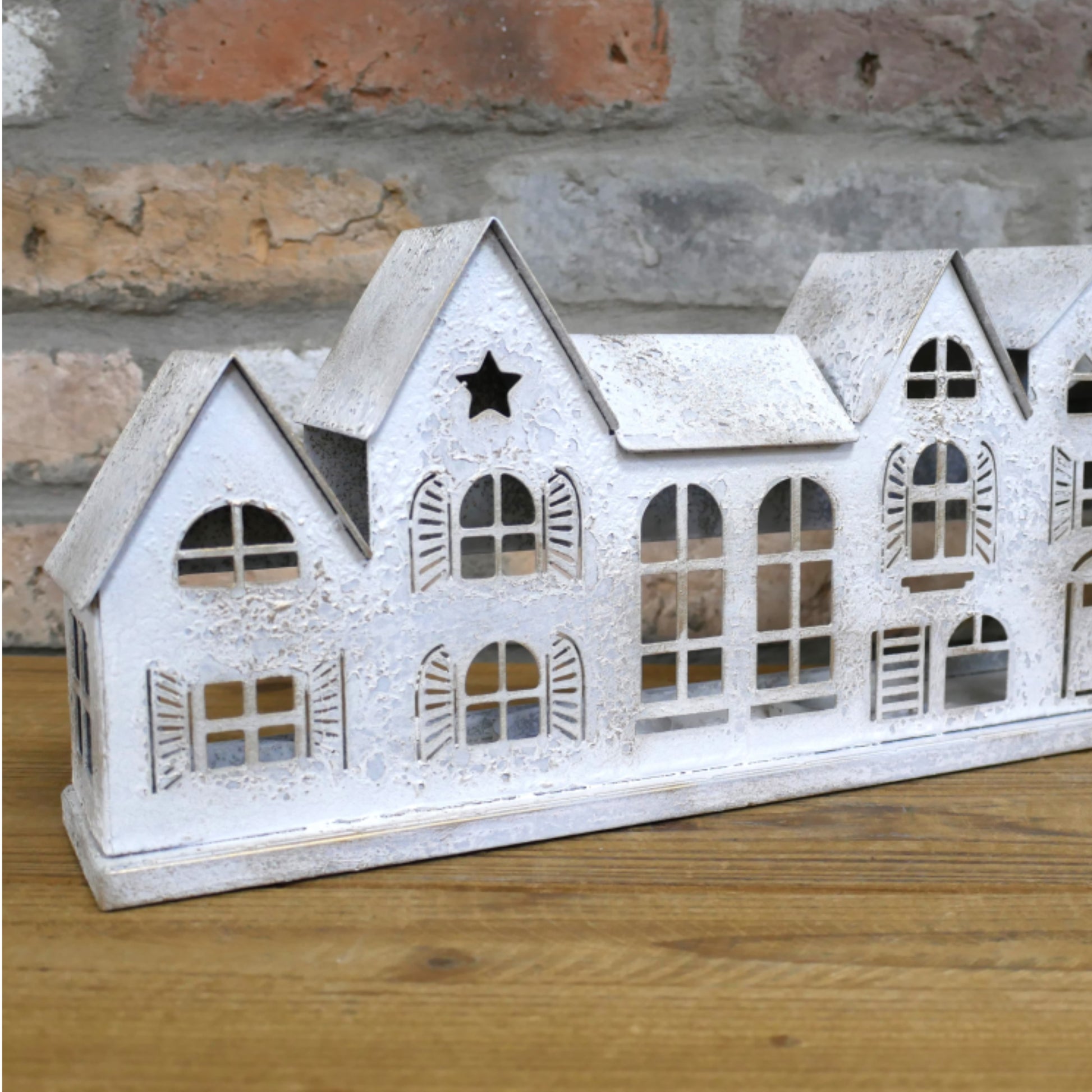 Decorative white house model on a wooden surface with a brick wall background