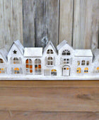 Decorative white house-shaped candle holder on a wooden surface with a stone wall background