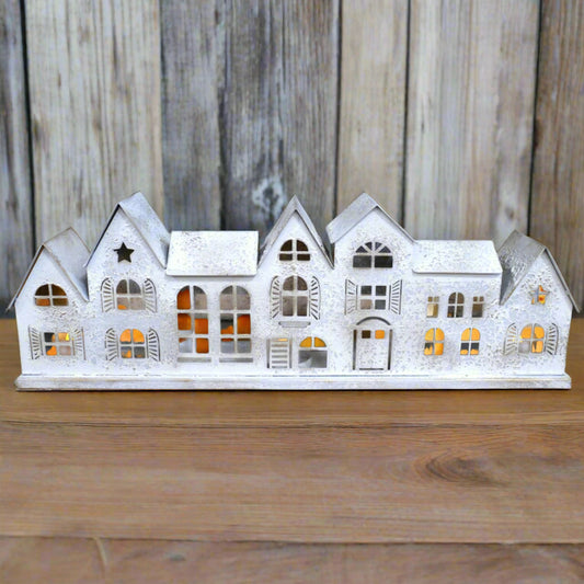 Decorative white house-shaped candle holder on a wooden surface with a stone wall background