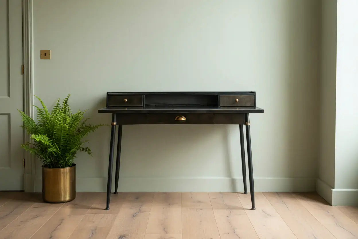 Dark wooden desk with brass accents against a light green wall.