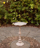 Decorative metal bird bath on a stone patio with greenery in the background