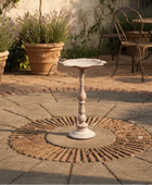 Decorative white pedestal table on a stone patio with potted plants and outdoor furniture in the background.