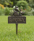 Decorative garden stake with a bird and tool design on a grassy background