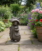 Statue of a garden gnome with a hat in a garden setting with flowers and plants.