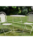 White metal garden table and chairs on grass with a garden background