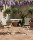 White metal outdoor table and chairs on a patio with wisteria and potted plants.
