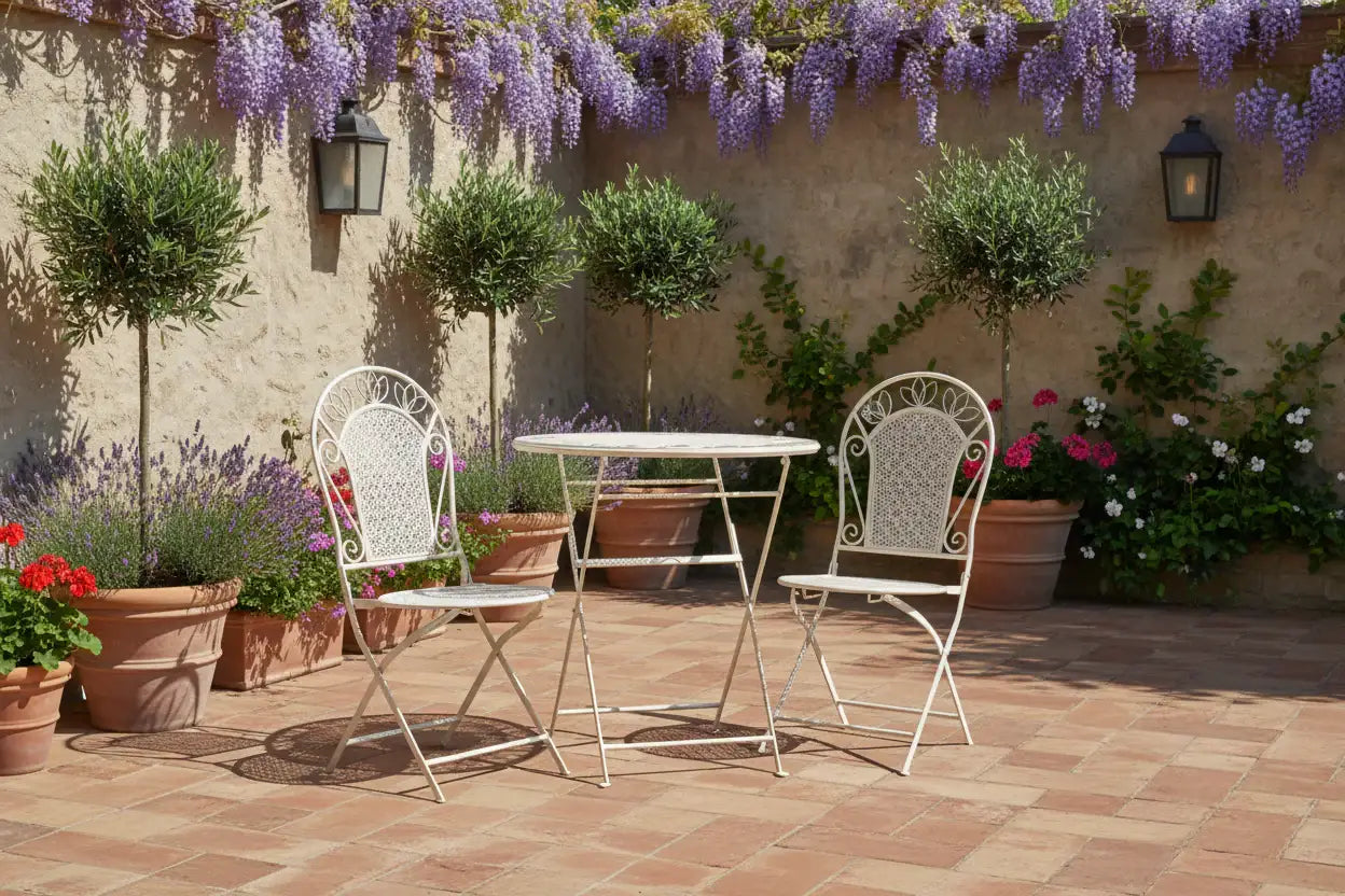 White metal outdoor table and chairs on a patio with wisteria and potted plants.