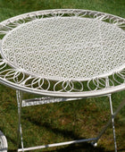 Decorative white metal table with intricate designs on a grassy background