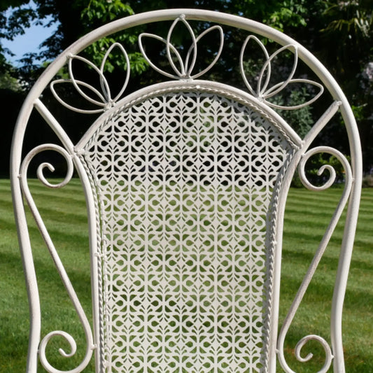 Decorative white metal chair with intricate patterns against a grassy background