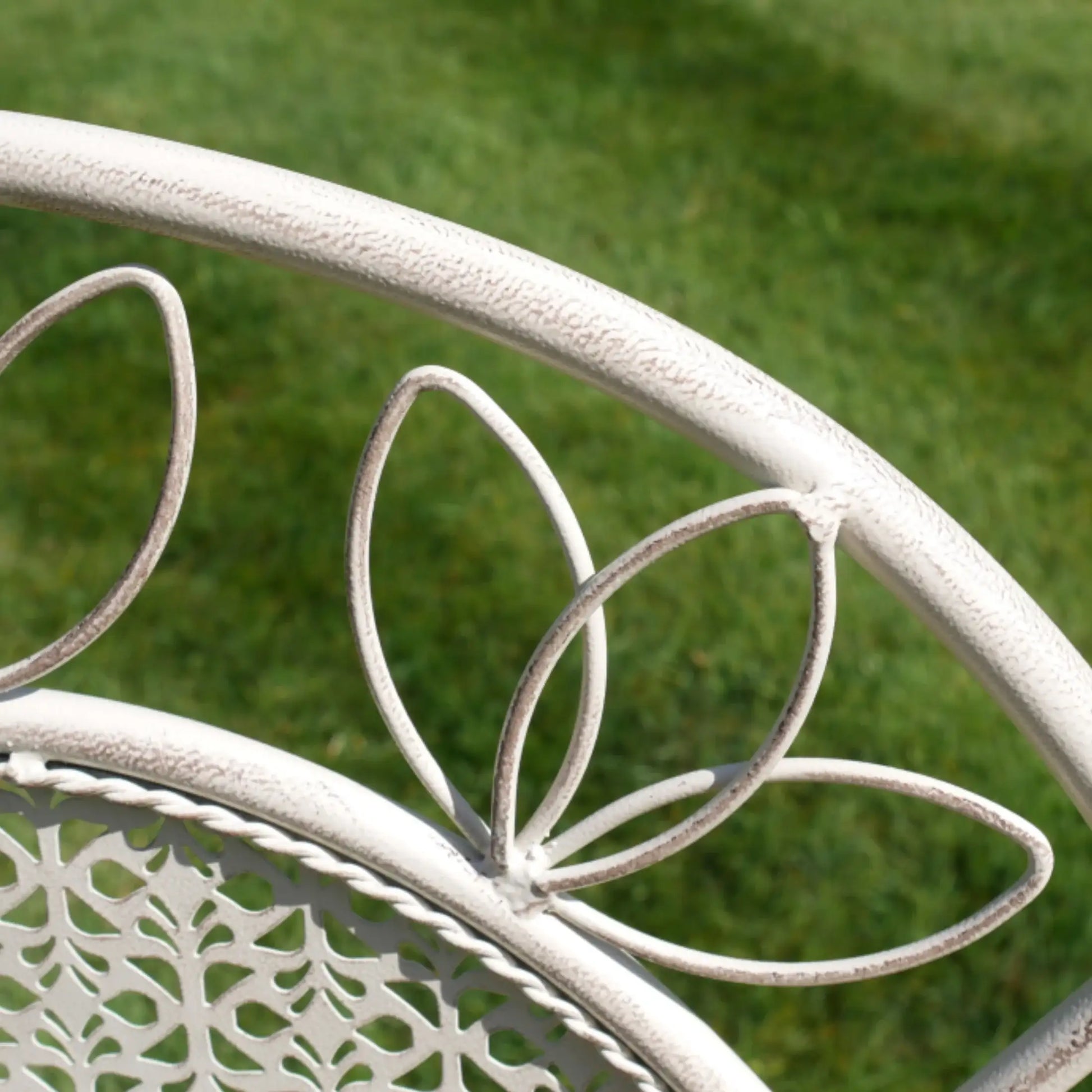 Close-up of a decorative metal chair with intricate designs against a grassy background