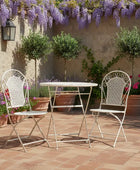 Outdoor patio set with table and chairs under a wisteria vine on a stone wall.