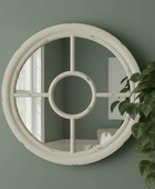 Round decorative mirror with a white frame on a green wall