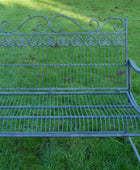 Wrought iron garden bench on grass with a fountain in the background