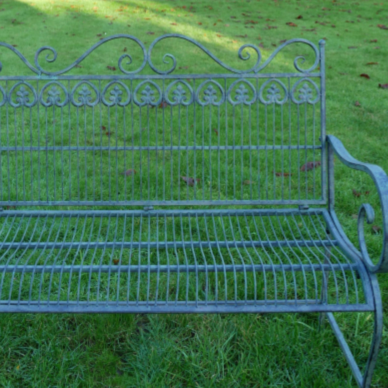 Wrought iron garden bench on grass with a fountain in the background