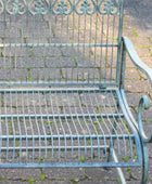 Decorative metal garden bench on a paved patio with greenery in the background