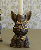 Bronze rabbit candle holder with glasses and a bow tie on a green surface.
