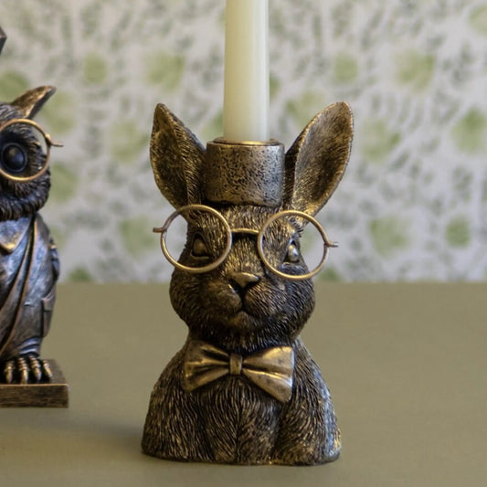 Bronze rabbit candle holder with glasses and a bow tie on a green surface.