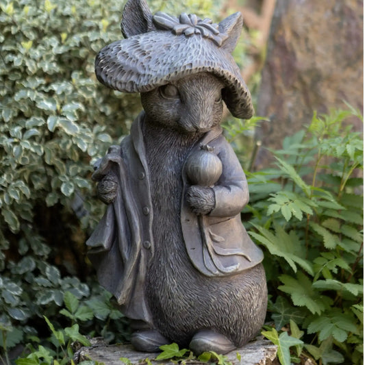 Statue of a rodent wearing a hat and coat, holding a mushroom, in a garden setting.