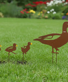 Metal duck family sculpture on grass with a garden in the background