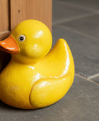 A glossy yellow rubber duck door stopper with an orange beak, resting against a dark gray cabinet on a wooden floor.