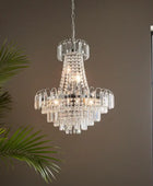 Crystal chandelier hanging against a neutral wall with a window and plant in the background
