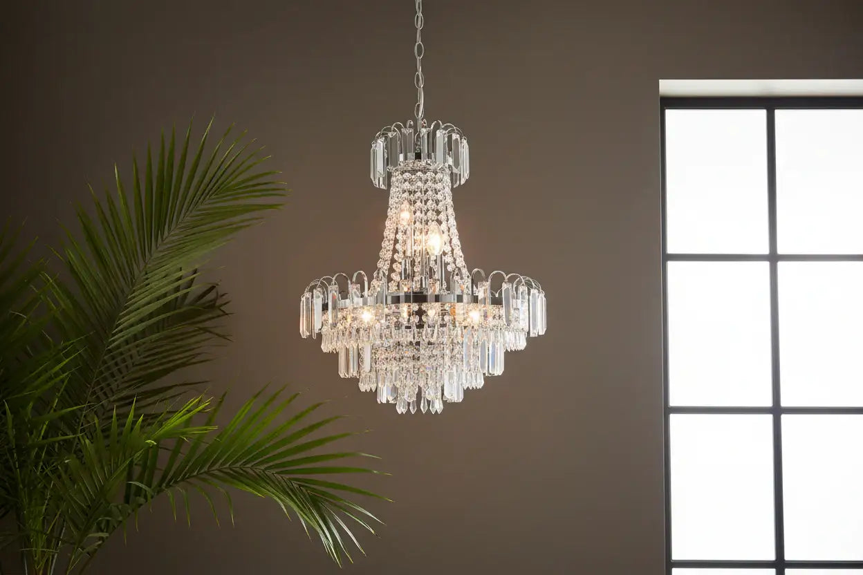 Crystal chandelier hanging against a neutral wall with a window and plant in the background