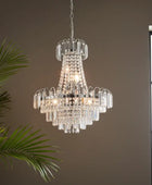 Crystal chandelier hanging against a neutral wall with a plant and window in the background