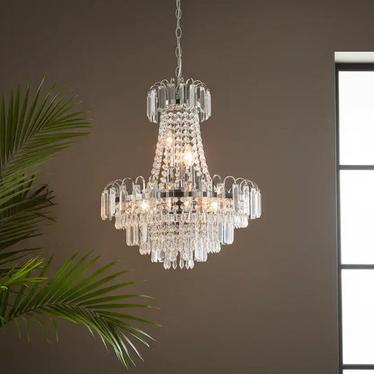 Crystal chandelier hanging against a neutral wall with a plant and window in the background