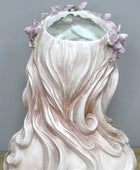 Vase shaped like a woman with long hair and flowers, on a neutral background