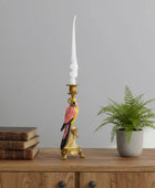 Decorative candlestick with parrot design on a wooden surface with books and a plant.