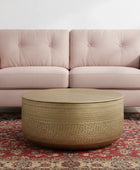 Pink sofa with a round woven coffee table on a patterned rug.