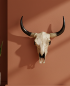 Bull skull with large horns on a brown wall next to a potted plant
